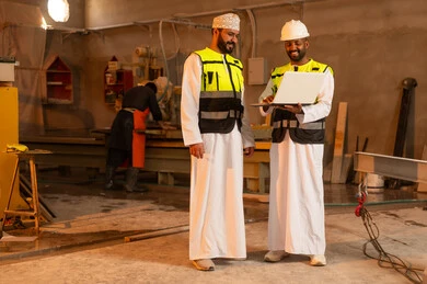 Home and office furniture manufacturing, two Omani Gulf Arab engineers wearing dishdashas and work clothes working on laptops, integrating technology into laboratories, workshops in the Sultanate of Oman, tools and equipment made of marble, quality of local national production