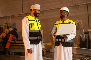Home and office furniture manufacturing, two Omani Gulf Arab engineers wearing dishdashas and work clothes working on laptops, integrating technology into laboratories, workshops in the Sultanate of Oman, tools and equipment made of marble, quality of local national production