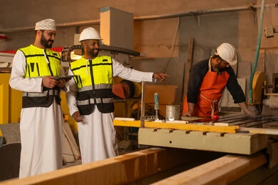 Monitoring and evaluating worker performance via tablet, factories and workshops in the Sultanate of Oman, marble manufacturing machines and equipment, quality of local national production, two Omani Gulf Arab engineers wearing dishdashas and work clothes working on tablets, integrating technology into factories