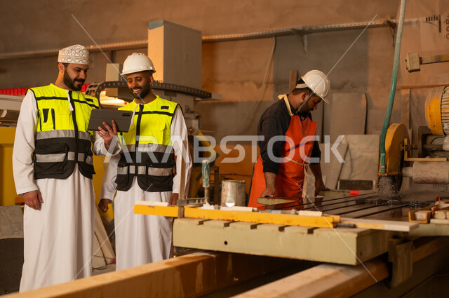 Monitoring and evaluating worker performance via tablet, factories and workshops in the Sultanate of Oman, marble manufacturing machines and equipment, quality of local national production, two Omani Gulf Arab engineers wearing dishdashas and work clothes working on tablets, integrating technology into factories