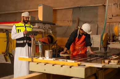 متابعة أداء العامل وتقيمه عبر التابلت، مصانع ومعامل سلطنة عمان, ألات ومكنات لصناعة الرخام، جودة الانتاج المحلي الوطني, رجل مهندس عربي خليجي عماني يرتدي الدشداشة وزي العمل يعمل على الجهاز اللوحي، دمج التقنية والتكنولوجيا في المعامل