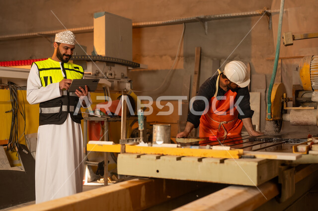 Monitoring and evaluating employee performance via tablet, factories and workshops in the Sultanate of Oman, marble manufacturing machines and equipment, quality of local national production, an Arab Gulf Omani engineer wearing a dishdasha and work clothes working on a tablet, integrating technology into factories.