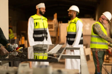 Exchange of views and experiences, workshops in the Sultanate of Oman, tools and equipment made of marble, quality of local national production, home and office furniture manufacturing, an Arab Gulf Omani engineer wearing a dishdasha and work clothes discussing with his colleague