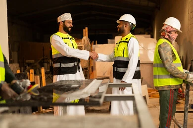 المصافحة والسلام والترحيب، ورشات عمل في سلطنة عمان, أدوات ومعدات مصنوعة من الرخام, جودة الانتاج المحلي الوطني, صناعة الأثاث المنزلي والمكتبي، رجل مهندس عربي خليجي عماني يرتدي الدشداشة وزي العمل يصافح زميله