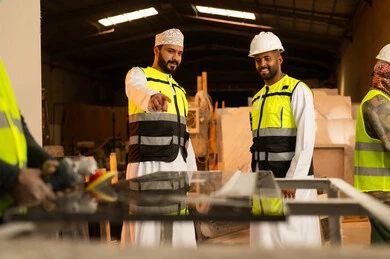 Pointing to something, workshops in the Sultanate of Oman, tools and equipment made of marble, quality of local national production, home and office furniture manufacturing, an Arab Gulf Omani engineer man wearing a dishdasha and work clothes standing inside the factory with his colleague