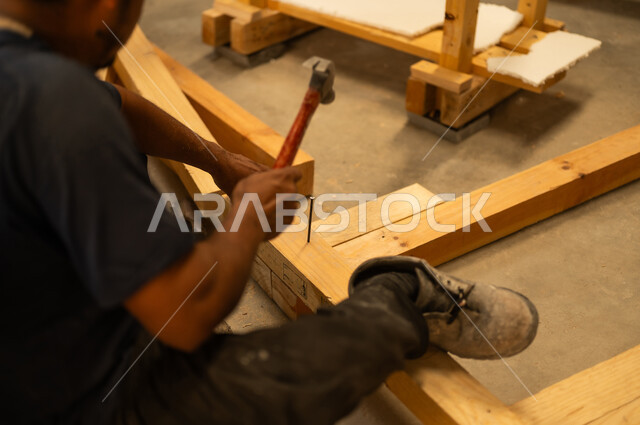 Traditional Saudi Arabian crafts and professions, workshop and factory, use of carpentry tools and equipment, close-up of a Saudi Arabian Gulf craftsman using a hammer and nail on a piece of wood in a carpentry shop