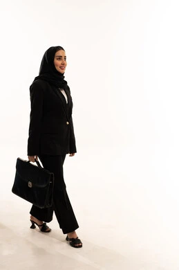 Carrying a handbag, a portrait of a veiled Saudi Arabian woman from the Gulf region wearing a black formal suit, standing upright, closing business deals, gestures of joy and happiness, feeling pleased with achieving company goals, white background