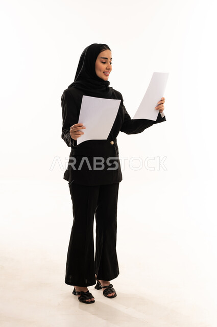 تدوين الملاحظات وإعداد التقرير اليومي، بورتيه لامرأة عربية سعودية خليجية محجبة ترتدي البدلة الرسمية السوداء تقف باستقامة تحمل بيدها مجموعة من الاوراق، مراجعة و متابعة الخطط و المشاريع, خلفية بيضاء