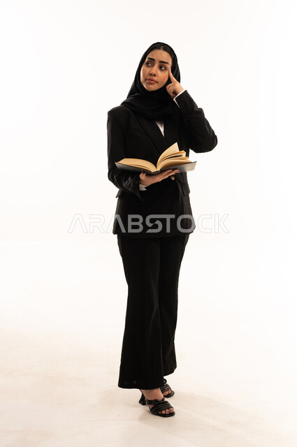 محاولة تذكر أمر معين, حب المطالعة والقراءة, قضاء أوقات الفراغ بالتثقيف والتعليم, بورتريه لامرأة عربية سعودية خليجية محجبة ترتدي البدلة الرسمية السوداء تقف باستقامة و تحمل كتاب, ثقافة التعلم الذاتي, خلفية بيضاء