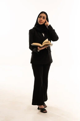 Trying to remember something specific, a love of reading, spending free time learning and educating, a portrait of a veiled Saudi Arabian woman from the Gulf wearing a black formal suit, standing upright and holding a book, a culture of self-learning, white background