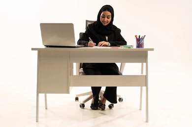 Work-related files and documents, office work being carried out within the company headquarters, a portrait of a veiled Saudi Arabian woman from the Gulf region wearing a black formal suit, sitting behind a desk with a laptop in front of her, studying projects and reviewing annual reports, white background