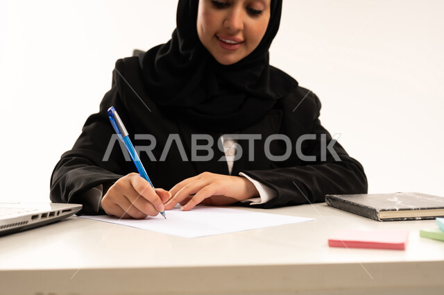 تدوين الأفكار وتسجيل المعلومات، مفهوم كتابه الملاحظات, بورتريه لامرأة عربية سعودية خليجية محجبة مبتسمة ترتدي البدلة الرسمية السوداء و  تمسك بيدها قلما وتقوم بالكتابة, مهن و وظائف نسائية، خلفية بيضاء