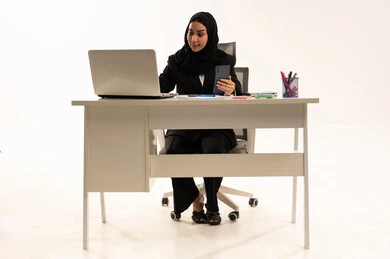 إرسال بريد الكتروني عبر الحاسوب, التواصل مع العملاء عن بعد, استخدام التقنيات الحديثة و المتطورة في العمل, بورتريه لامرأة عربية سعودية خليجية محجبة ترتدي البدلة الرسمية السوداء تستخدم اللابتوب و تحمل الموبايل, خلفية بيضاء