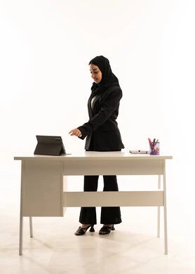 منصات التعليم المتطورة، بورتريه لمعلمه عربيه سعوديه خليجيه محجبة ترتدي البدله الرسميه السوداء تقف امام مكتب ابيض و تستخدم جهاز التابلت, جودة أساليب التعلم الفعال, خلفية بيضاء