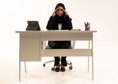 إيجاد حل لمشكلة ما,  بورتريه لامرأة عربية سعودية خليجية تجلس خلف المكتب ترتدي البدلة الرسمية السوداء و تستخدم التابلت و تضع يدها على رأسها في حيرة, ايماءات التمعن و الاندماج, خلفية بيضاء