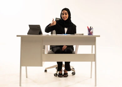 Gestures of approval and acceptance, integrating work with modern technology, a portrait of a veiled Saudi Arabian woman from the Gulf sitting behind a desk wearing a black formal suit, using a tablet and raising her thumbs in a like sign, white background.