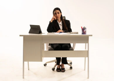 العمل ضمن مقر الشركة، التفكير في الاستراتيجيات والأهداف, بورتريه لامرأة عربية سعودية خليجية تجلس خلف المكتب ترتدي البدلة الرسمية السوداء و تستخدم التابلت, ايماءات الحيرة و الاندماج, خلفية بيضاء