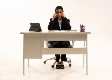 Thinking about strategies and goals, working within the company headquarters, a portrait of a Saudi Arabian Gulf woman sitting behind a desk wearing a black formal suit, using a tablet and resting her hand on her head in apparent bewilderment, gestures of contemplation and absorption, white background