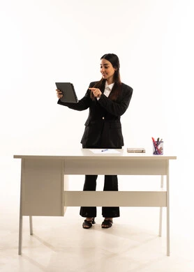 النقر على شاشة الجهاز اللوحي, تنمية و تطوير المهارات، التعليم المتطور في مدارس المملكة العربية السعودية, بورتريه لمعلمه عربيه سعوديه خليجيه ترتدي البدله الرسميه السوداء تقف امام مكتب ابيض و تحمل جهاز التابلت, خلفية بيضاء