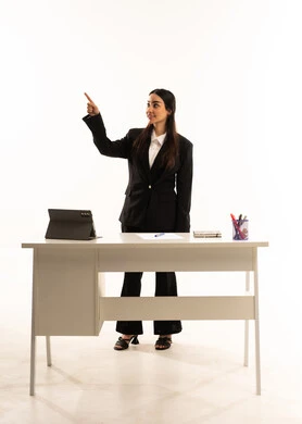 The quality of education in Saudi Arabia: A portrait of a Saudi Arabian teacher wearing a black formal suit, standing in front of a white desk, raising her index finger to point at something. Explaining and teaching using a tablet. Full-length portrait, white background. The quality of education in Saudi Arabia: A portrait of a Saudi Arabian teacher wearing a black formal suit, standing in front of a white desk, raising her index finger to point at something. Explaining and teaching using a tablet. Full-length portrait, white background.
