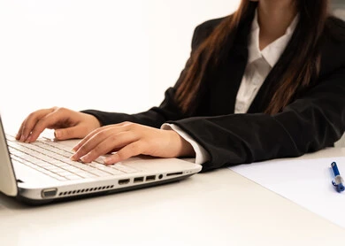 النقر على لوحة المفاتيح, دمج العمل مع التكنولوجيا الحديثة، إجراء الاعمال المكتبيه داخل مقر الشركه عبر اللابتوب، بورتريه مقرب ليد امرأة عربية سعودية خليجية ترتدي البدلة الرسمية السوداء و تستخدم الحاسب المحمول, خلفية بيضاء