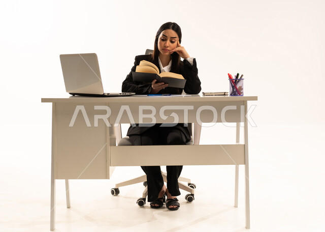 Reading, studying, and project planning; performing office tasks and work within the company headquarters; a portrait of a Saudi Arabian woman from the Gulf region wearing a black formal suit, sitting behind a desk and reading with focused and thoughtful gestures; white background.