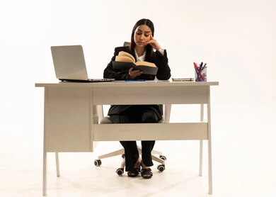 القراءة و المطالعة و دراسة المشروع، إجراء المهام والاعمال المكتبيه داخل مقر الشركه، بورتريه لامرأة عربية سعودية خليجية ترتدي البدلة الرسمية السوداء تجلس خلف المكتب و تقرأ بإيماءات التركيز والتمعن،  خلفية بيضاء