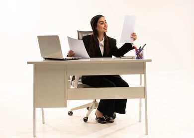 Reading the contract clauses, engrossed in work, performing office tasks and duties within the company premises, a portrait of a Saudi Arabian Gulf woman wearing a black formal suit, sitting behind a desk holding papers, studying projects and reviewing annual reports, white background