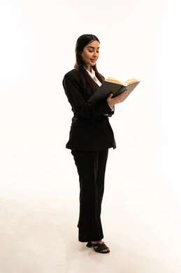 ممارسة هواية المطالعة، ايماءات التركيز والاستمتاع، قراءة الروايات والقصص، تمضية وقت الفراغ بالتعلم والتثقيف الذاتي، بورتريه لامرأة عربية سعودية خليجية مبتسمة ترتدي البدلة الرسمية السوداء تقف باستقامة و تحمل بيدها كتاب, خلفية بيضاء