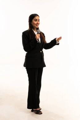 مفهوم الفن وتأثيره الايجابي على الامرأة، تقديم العروض الفنيه و الغنائيه والفقرات الترفيهية، بدء التدريب الصوتي، بورتريه لامرأة عربية سعودية خليجية مبتسمة ترتدي البدلة الرسمية السوداء تقف باستقامة و تمسك بيدها المايكروفون بإيماءات الاندماج, خلفية بيضاء