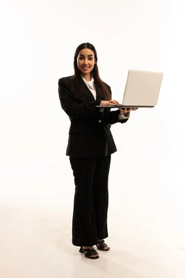 استخدام اللابتوب في تنظيم خطط العمل، استخدام الأجهزة التقنية الحديثة في إنجاز المهام، بورتريه لامرأة عربية سعودية خليجية مبتسمة ترتدي البدلة الرسمية السوداء تقف باستقامة و تستخدم الحاسب المحمول, خلفية بيضاء