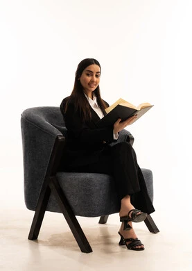 الاستمتاع بمطالعة الكتب والقصص والروايات, قضاء الوقت بالقراءة والتعلم والتثقف، بورتيه لامرأة عربية سعودية خليجية ترتدي البدلة الرسمية السوداء تجلس على كرسي مريح و تحمل بيدها  كتاب، ثقافة التعلم الذاتي, خلفية بيضاء