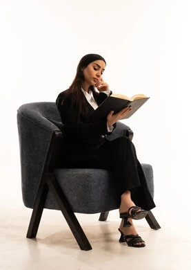 هواية القراءة والاستكشاف، الاستمتاع بالكتب والقصص والروايات، بورتيه لامرأة عربية سعودية خليجية ترتدي البدلة الرسمية السوداء تجلس على كرسي مريح و تحمل بيدها  كتاب، ثقافة التعلم الذاتي, خلفية بيضاء