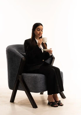 Spending a pleasant and quiet time, sitting and enjoying hot drinks and warm winter herbs, sipping your favorite beverage. Portrait of a Saudi Arabian Gulf woman wearing a black formal suit, sitting in a comfortable chair and holding a cup of tea, white background.
