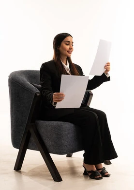 Using white paper to record important notes and information; tools for writing down daily tasks; gestures of happiness and optimism; a portrait of a Saudi Arabian woman wearing a black formal suit, sitting in a comfortable chair, holding a stack of papers; reviewing and following up on plans and projects; white background.