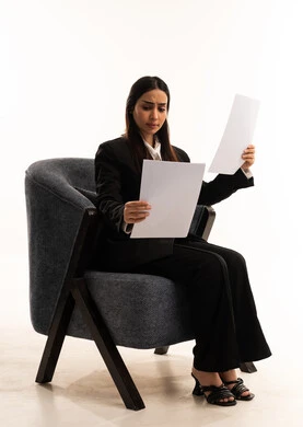 Tools for taking daily notes, using white paper to record important information, gestures of focus and contemplation, a portrait of a Saudi Arabian woman wearing a black formal suit, sitting in a comfortable chair and holding a stack of papers, reviewing and following up on plans and projects, white background.