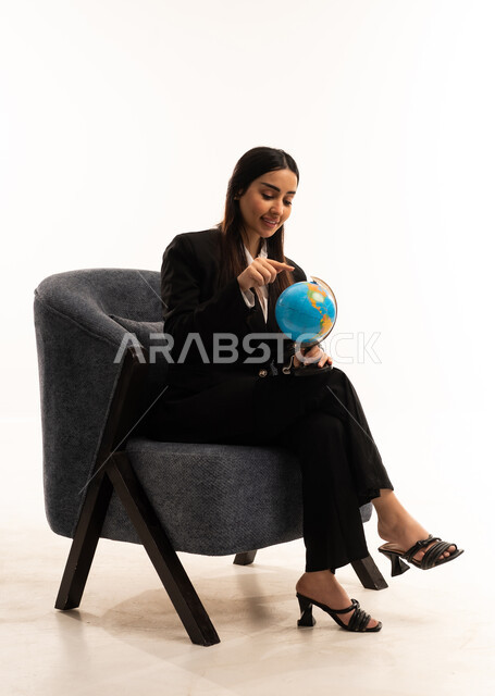 The image features a globe, symbolizing elegance and attention to appearance; a portrait of a Saudi Arabian woman from the Gulf region wearing a black formal suit and sitting in a comfortable chair;  research and exploration around the world, set against a white background.