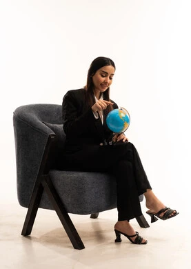 The image features a globe, symbolizing elegance and attention to appearance; a portrait of a Saudi Arabian woman from the Gulf region wearing a black formal suit and sitting in a comfortable chair;  research and exploration around the world, set against a white background.