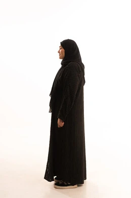 Elegance and attention to appearance, standing straight and looking at something, side portrait of a veiled Saudi Arabian Gulf woman wearing a black abaya standing with self-confident gestures, full-length body image, white background