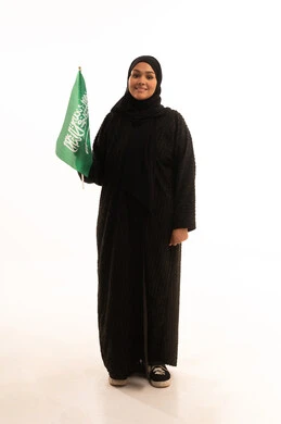 Saudi National Day commemoration, September 23, Flag Day, March 11, the concept of love and belonging to one's homeland, a portrait of a smiling, veiled Saudi Arabian Gulf woman wearing a black abaya, holding the Kingdom's flag in her hand and looking at the camera with gestures of pleasure and self-confidence, a full body image, a white background