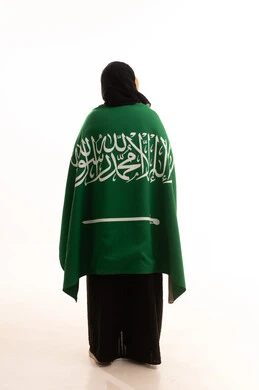 Love and loyalty to the country, looking up with gestures of pride and honor of belonging to the homeland, Saudi National Day September 23, Flag Day March 11, portrait from the back of a veiled Saudi Arabian Gulf woman wearing an abaya with the flag of the Kingdom on her shoulders, full body image, white background