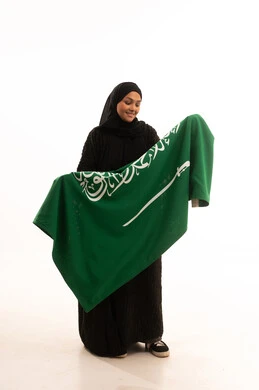 Looking at the flag with gestures of pride and belonging to the homeland, Saudi National Day, September 23, Flag Day, March 11, showing love and loyalty to the country, portrait of a veiled Saudi Arabian Gulf woman wearing a black abaya holding the flag of the Kingdom, full body image, white background
