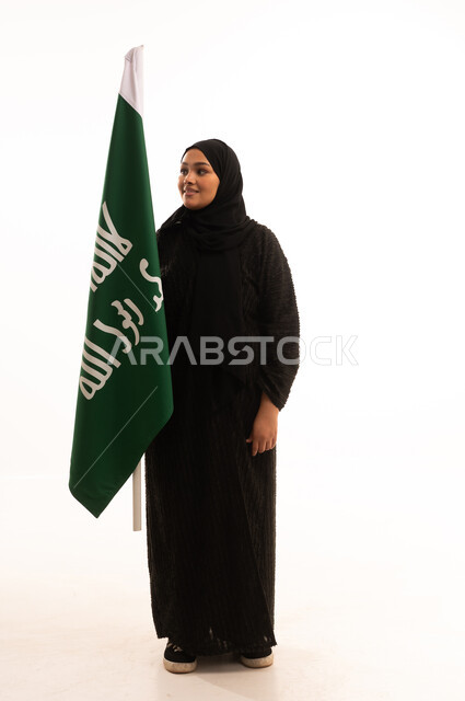 Commemorating the founding of the first Saudi state in 1727 AD, pride in the achievements of the Kingdom, the day we began, February 22, showing loyalty and love for the homeland, portrait of a Saudi Arabian Gulf woman wearing a hijab and abaya holding the founding flag with gestures of pride and loftiness, full-length body, white background