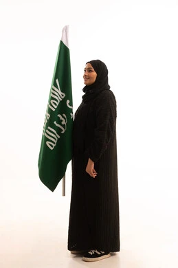 Pride in the Kingdom's achievements, the day we began, February 22, the anniversary of the founding of the first Saudi state in 1727 AD, showing loyalty and love for the homeland, a side portrait of a Saudi Arabian Gulf woman wearing a hijab and abaya holding the founding flag with gestures of pride and loftiness, full-length body, white background
