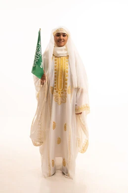 التباهي بإنجازات البلاد، النظر الى الكاميرا بتعابير الفخر، اليوم الوطني السعودي 23 سبتمبر، يوم العلم 11 مارس، بورتريه لامرأة عربية خليجية سعودية مبتسمة ترتدي الشيلة والنشل تحمل بيدها علم المملكة، ارتداء أزياء المنطقة الشرقية، الجسم الكامل بالطول، خلفية بيضاء