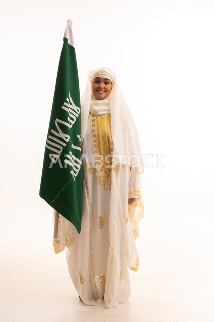 الاحتفال بالأعياد الوطنية الشعبية، ارتداء أزياء المنطقة الشرقية، يوم العلم السعودي11 مارس، يوم بدينا 1727 م، بورتريه لإمرأة عربية خليجية سعودية مبتسمة ترتدي الشيلة والنشل تحمل بيدها علم يوم تأسيس الدولة السعودية الأولى، الجسم بالطول الكامل، خلفية بيضاء