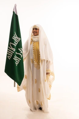 Wearing the costumes of the Eastern Province, Saudi Flag Day, March 11, the day of our beginnings, 1727 AD, a portrait of a smiling Saudi Arabian Gulf woman wearing a sheila and a neshul holding the flag of the founding day of the first Saudi state, celebrating popular national holidays, full-length body, white background