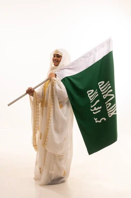 يوم بدينا 1727 م، الاحتفال بالأعياد الوطنية الشعبية، ارتداء أزياء المنطقة الشرقية، يوم العلم السعودي11 مارس، بورتريه من الجانب لإمرأة عربية خليجية سعودية مبتسمة ترتدي الشيلة والنشل تحمل بيدها علم يوم تأسيس الدولة السعودية الأولى، الجسم بالطول الكامل، خلفية بيضاء