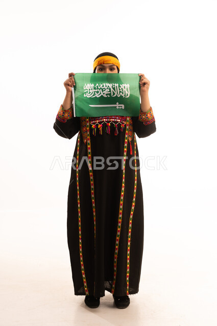 يوم بدينا 1727م, الاعتزاز والتباهي بإنجازات البلاد، الفخر بالتراث التاريخي، يوم العلم 11 مارس، ارتداء زي المنطقة الوسطى، اليوم الوطني السعودي 23 سبتمبر, بورتريه لإمرأة عربية خليجية سعودية ترتدي الكرتة والهامة تحمل علم المملكة, الجسم بالطول الكامل، خلفية بيضاء