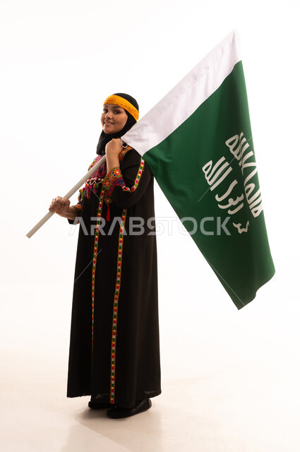 الاحتفال بالمناسبات والأعياد الوطنية الشعبية، ذكرى تأسيس الدولة السعودية الأولى 22 فبراير، يوم بدينا 1727 م، ارتداء أزياء المنطقة الوسطى، بورتريه لإمرأة عربية خليجية سعودية مبتسمة ترتدي الكرتة والهامة تحمل بيدها علم يوم التأسيس، الجسم بالطول الكامل، خلفية بيضاء
